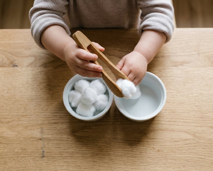 Toddler fine motor activity using salad tongs to move cotton balls between bowls